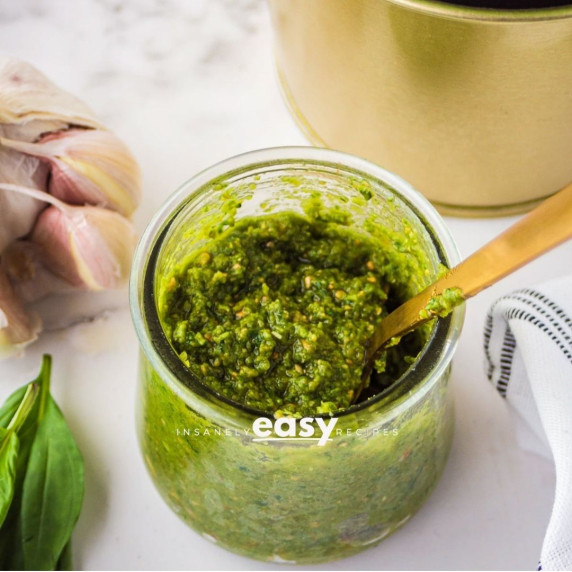 Nut free pesto sauce with sunflower seeds in a glass container with a spoon, garlic bulb on the side