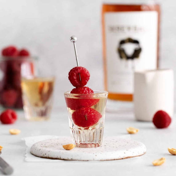 Peanut butter and jelly shot in a shot glass with raspberries skewered in a cocktail pick