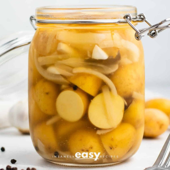 pickled potatoes in a glass jar on a white surface