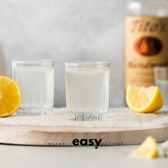 Two shot glasses of White Tea Shot on a wooden board, with lemon slices on the sides