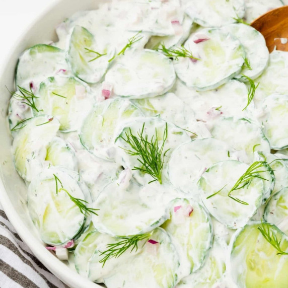 Mizeria or thinly sliced cucumber salad with sour cream, topped with fresh dill in a white bowl