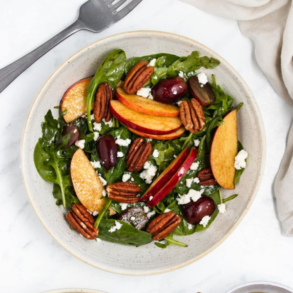 Salad with pecans and apple slices, sprinkle with feta cheese on a whote plate, a fork next to it