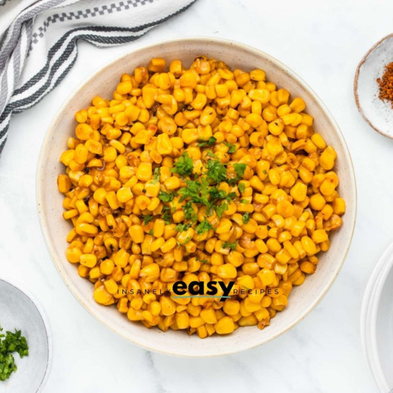 Fried corn topped with fresh chopped herbs in a white bowl