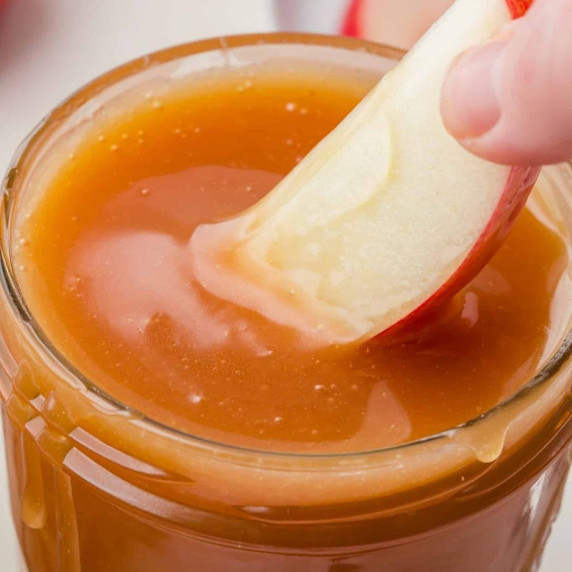 Apple slice dipped into a caramel sauce in a glass jar