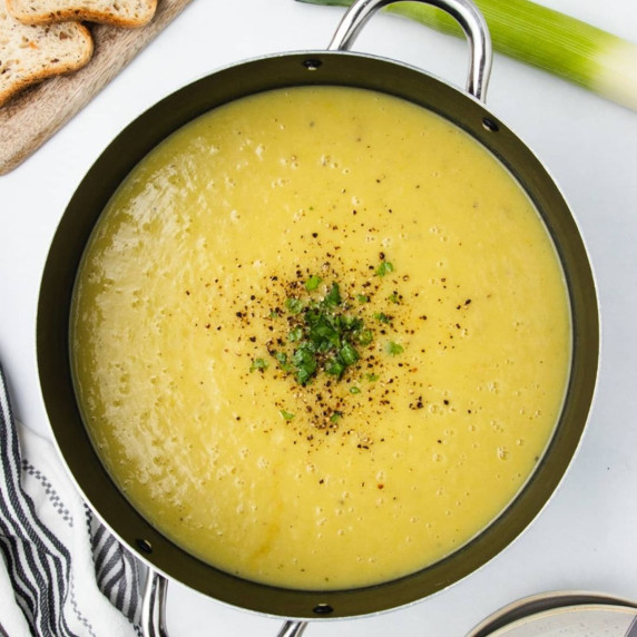 Magic leek soup topped with chopped green herbs and ground pepper in a stainless steel pot 