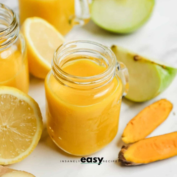 Ginger turmeric shot in a small glass jar surrounded with lemon, turmeric, and green apple slices