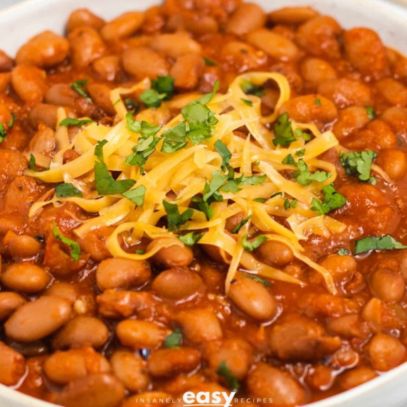 Pinto beans topped with shredded cheese and chopped cilantro in a white bowl