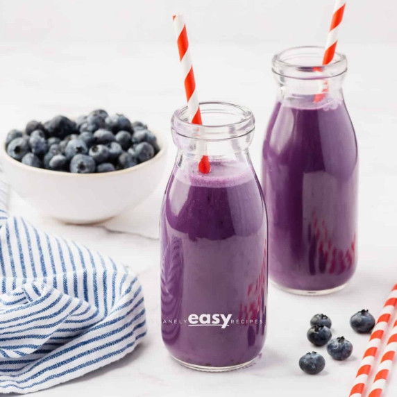 Blueberry milk in two glasses with straws, some fresh blueberries on the sides