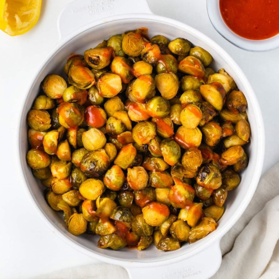 Roasted brussel sprouts drizzled with sriracha sauce in a white pot 