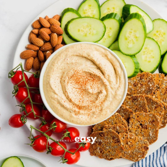 Bitchin sauce in a white bowl served with crackers, almonds, cherry tomatoes, and sliced vegetables