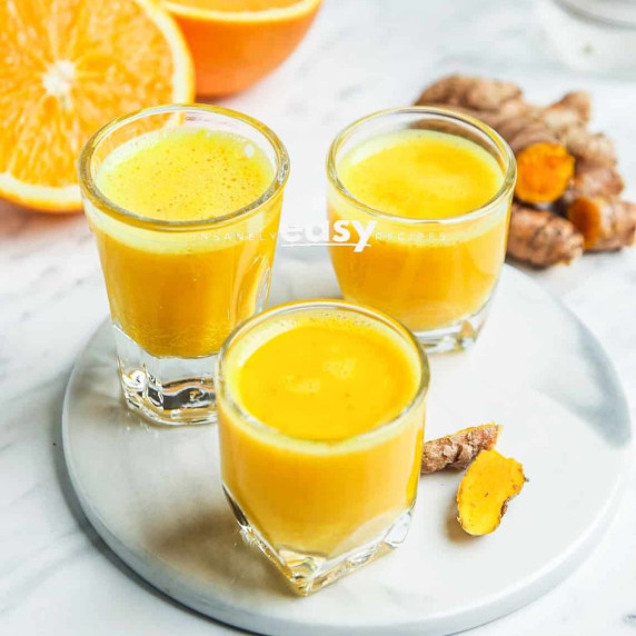 Turmeric shot in shot glasses, fresh turmeric and oranges nearby