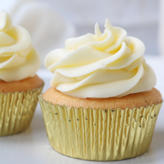 Cupcake decorated with swirled piped white buttercream in a gold case sitting on a grey counter