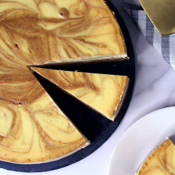 Vanilla Bean Cajeta Goat Cheese Cheesecake with a slice removed on a black serving platter
