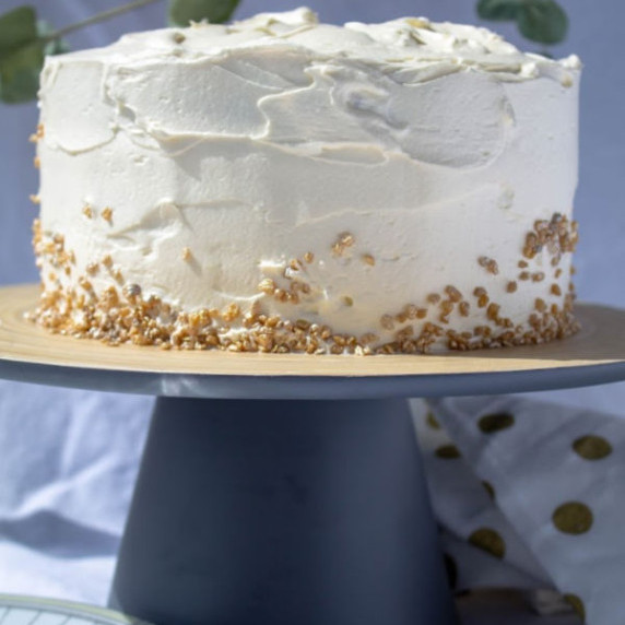 round, three-layer vanilla cake with gold sprinkles on a gray wood stand