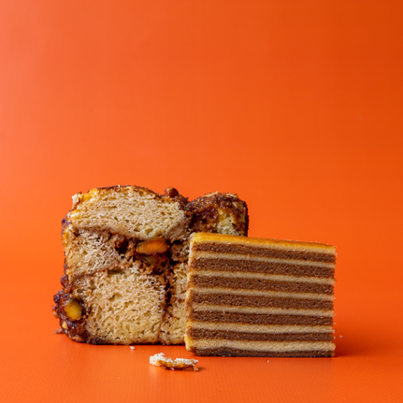 A slice of Indonesian thousand layer cake with a slice of vegan monkey bread on an orange backdrop.