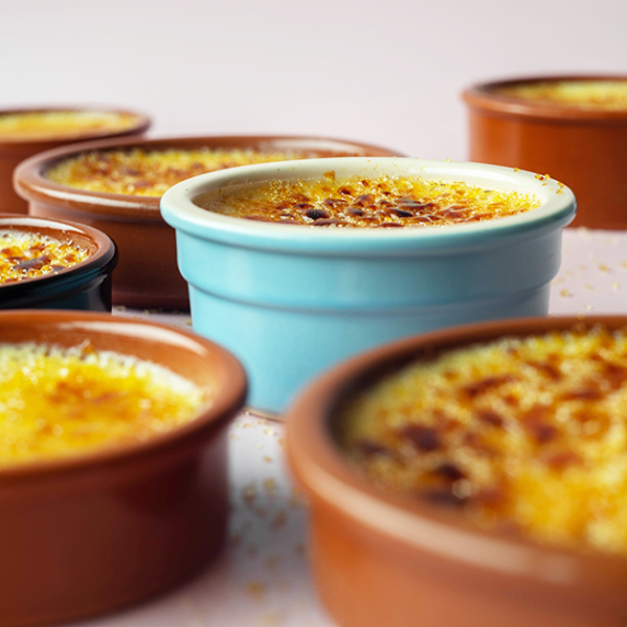 A variety of crème brûlée pots in terracotta and blue on a soft pink background.