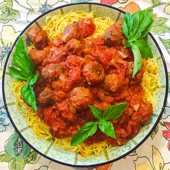 A bowl of pasta with basil and marinara sauce, with Vegan Eggplant Meatballs on top.