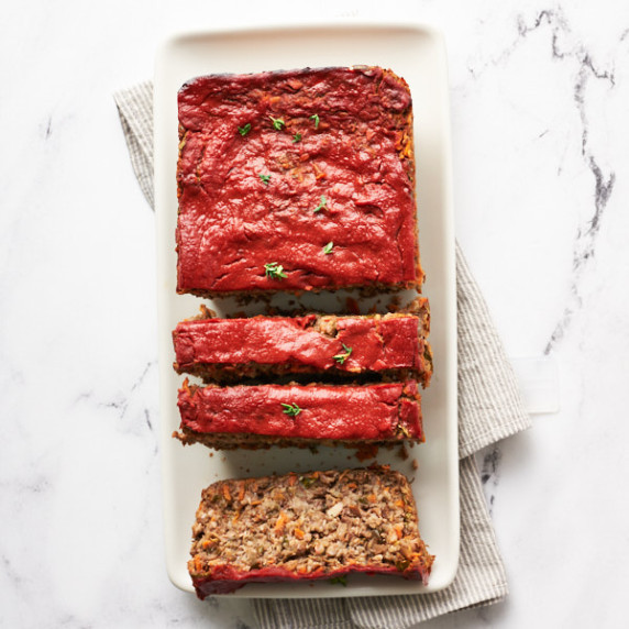 Sliced vegan meatloaf on a white platter on a marble background with grey striped napkin