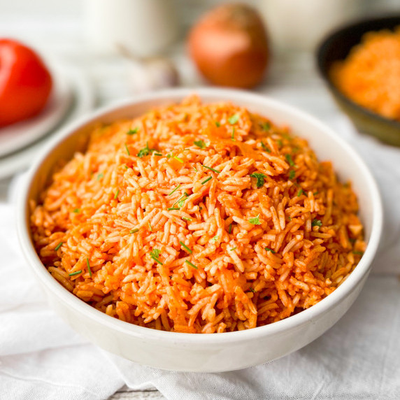 A white bowl with Mexican rice. The ingredients can be seen out of focus behind.