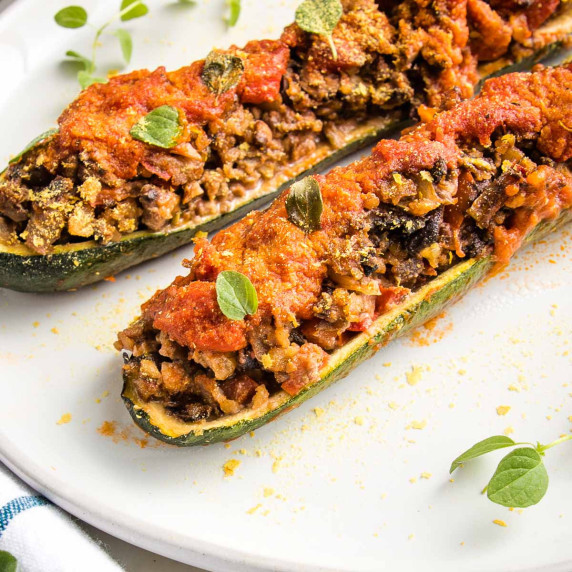 Close up of meaty vegan stuffed zucchini boats on a white plate, sprinkled with fresh oregano leaves