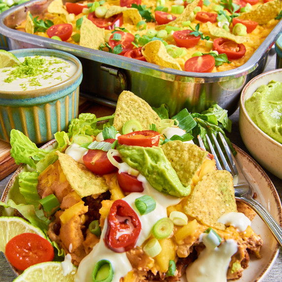 Vegan Taco Casserole topped with guacamole, crema, tortilla chips, spring onions, lettuce, jalapeno