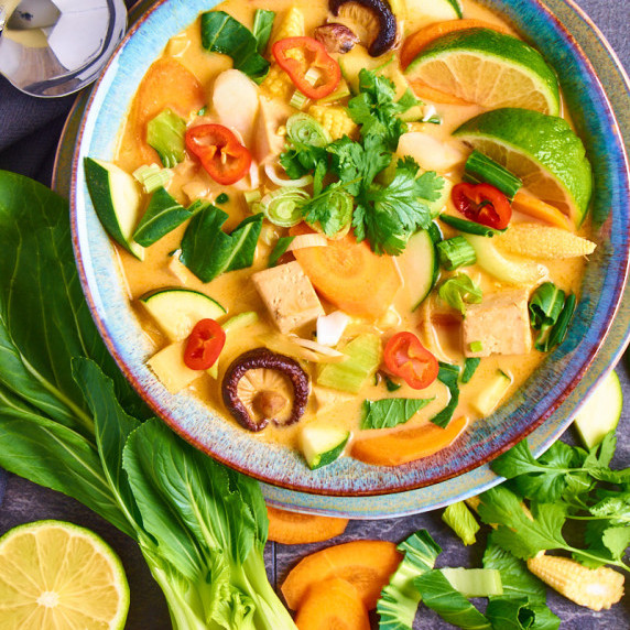 A bowl with Vegan Tom Kha Soup showing different vegetables, tofu and herbs.