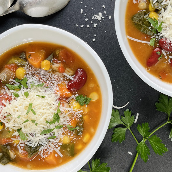 Two bowls of vegetable barley soup topped with parmesan cheese and minced parsley.