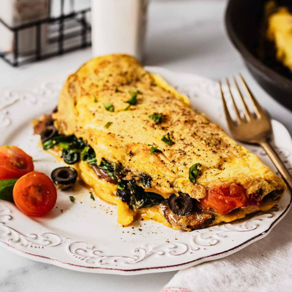 Vegetable omelette with spinach, tomatoes and black olives on a white plate with a gold fork.