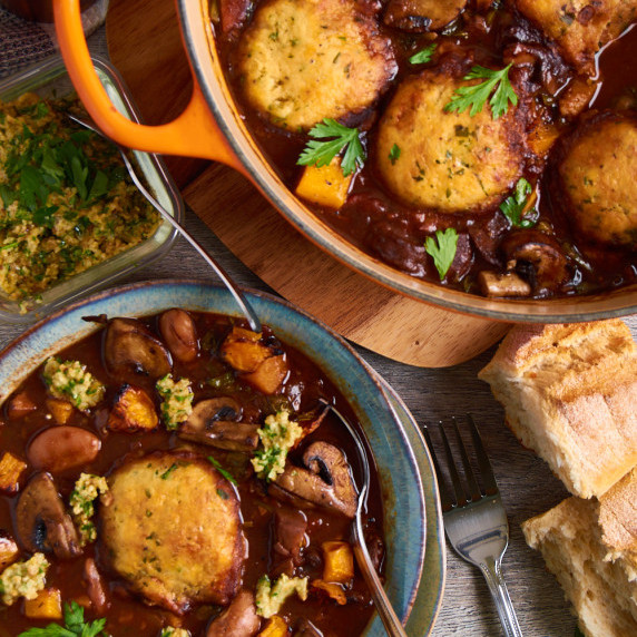 A pot and bowl filled with Vegetable Stew with Dumplings. Topped with Gremolata and fresh parsley.