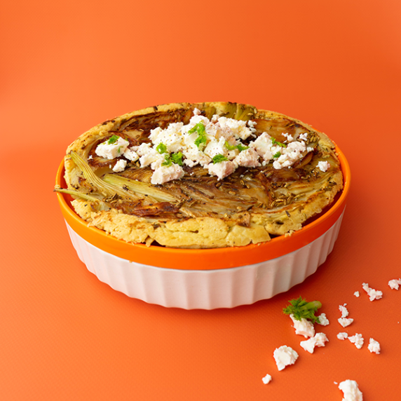 A plate of fennel tarte tatin in a classic quiche dish on an orange backdrop