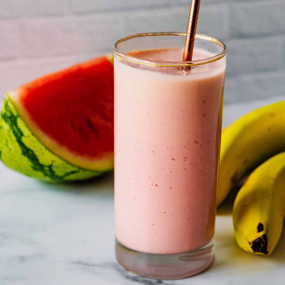 Watermelon banana smoothie in a tall glass with a slice of watermelon and bunch of bananas