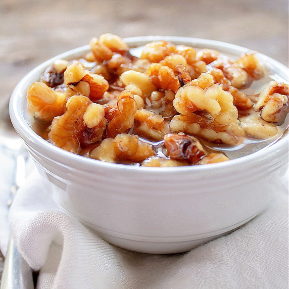 Walnuts in a delicious sauce in a white bowl on tp of a white linen napkin