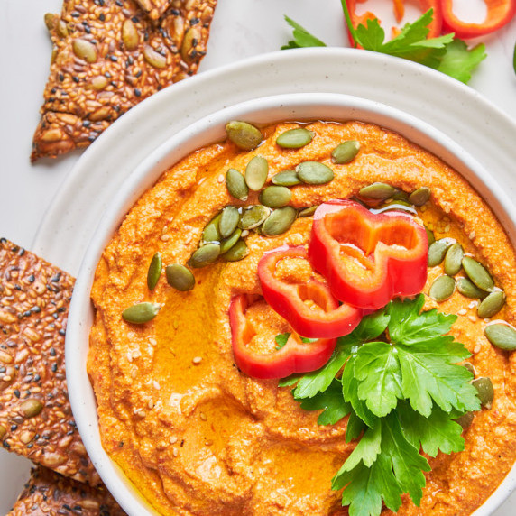 Whipped Red Pepper Tofu Dip in a white bowl, surrounded by crackers, topped with parsley and peppers