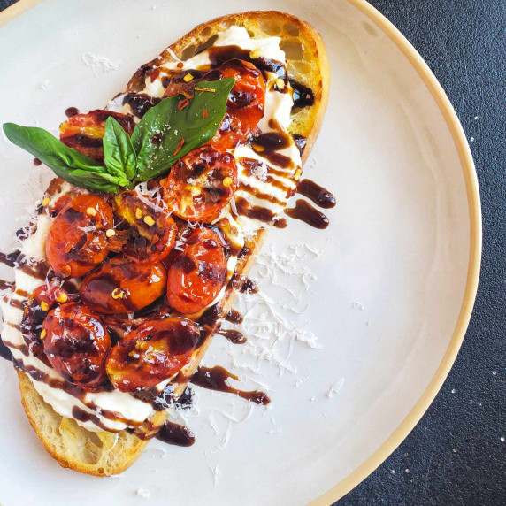 Golden brown toast, white ricotta, bright red tomatoes, and a black balsamic drizzle.