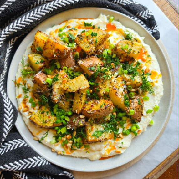 Golden potatoes piled with green herbs on a bed of white cheese.