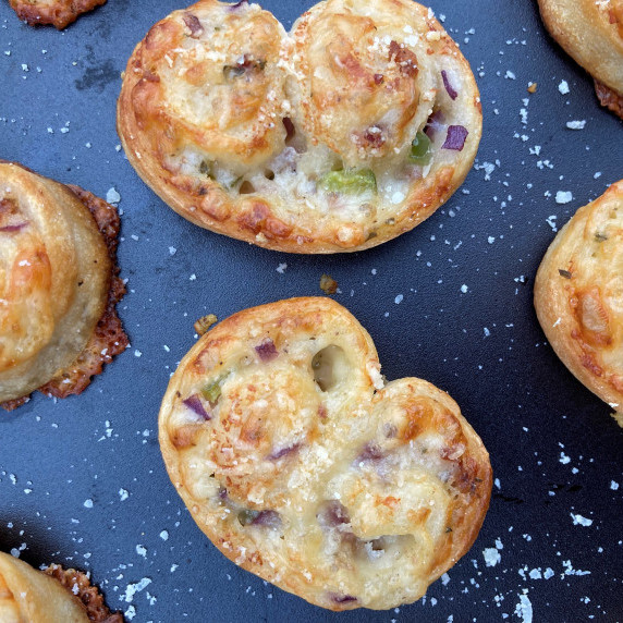 Cheesy palmiers on a black plate sprinkled with grated parmesan cheese.