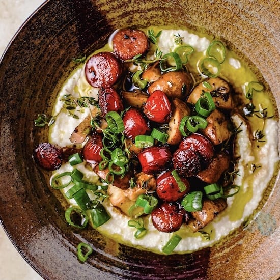 Grits, sausage and green onions in a brown stoneware bowl
