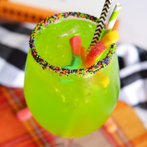 green cocktail in wine glass with candy worms and halloween sprinkles on the rim
