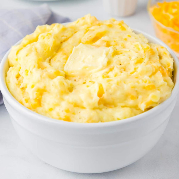 A large bowl filled with Yukon Gold mashed potatoes topped with a melty pat of butter.