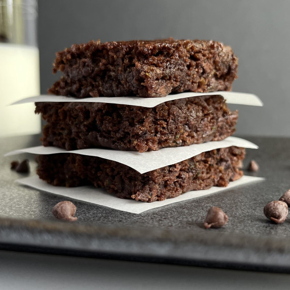 Three chocolate brownies in a stack on a black plate with chocolate chips. 