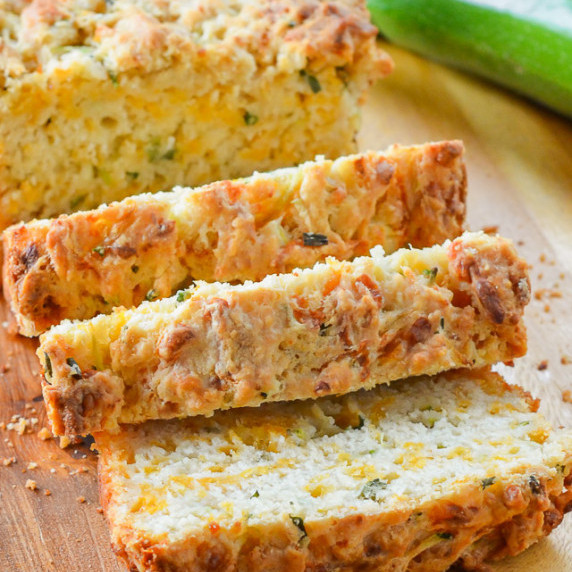 Sliced Zucchini Cheddar Cheese Herb Beer Bread on a wooden cutting board.