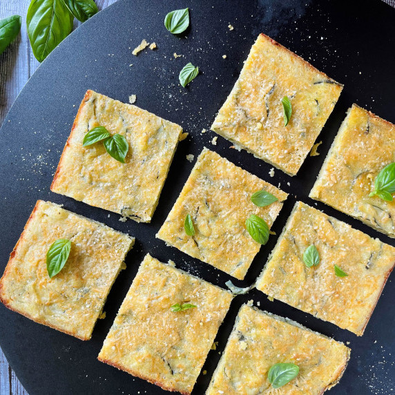 Slices of a zucchini tart garnished with fresh basil leaves on a black platter. 