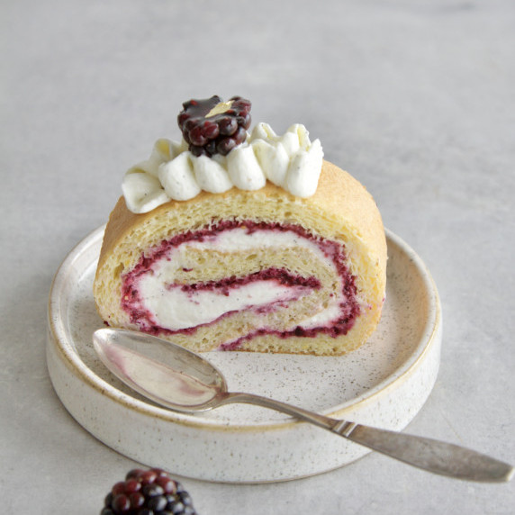 A slice of blackberry vanilla Swiss roll cake on a small place with a spoon