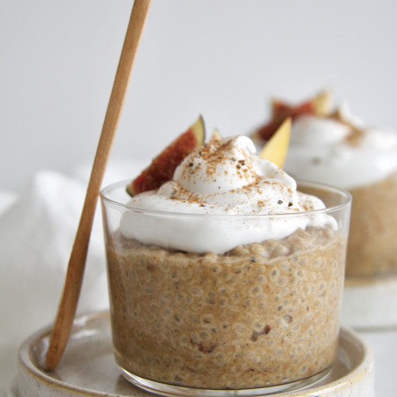 Glass filled with pumpkin spiced chia pudding with a dollop of cream and pinch of spice