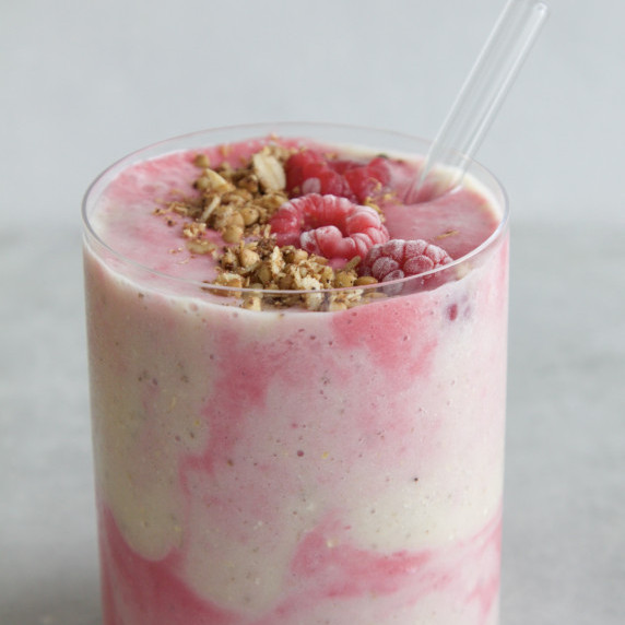 Glass with swirled raspberry and banana fruit smoothie with homemade granola on top.