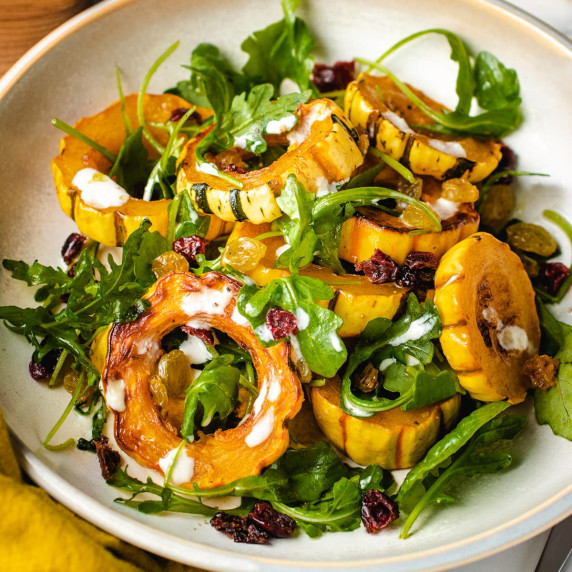 Roasted squash with cranberries and greens on a white plate