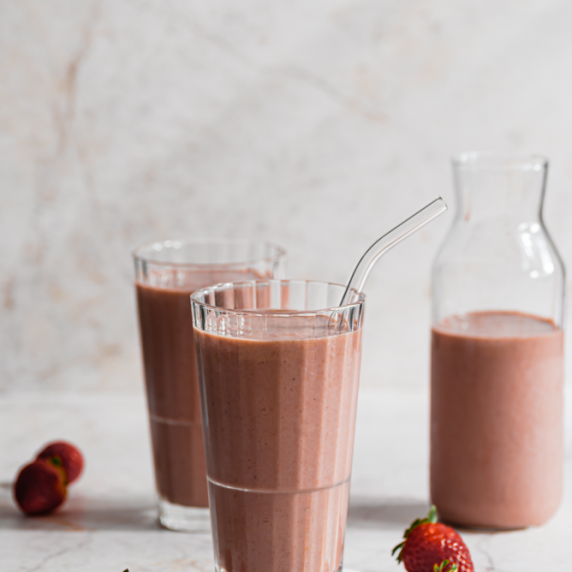 Super Berry Camu Camu Smoothie arranged in a 2 aesthetic cups with straw and strawberries on the sid