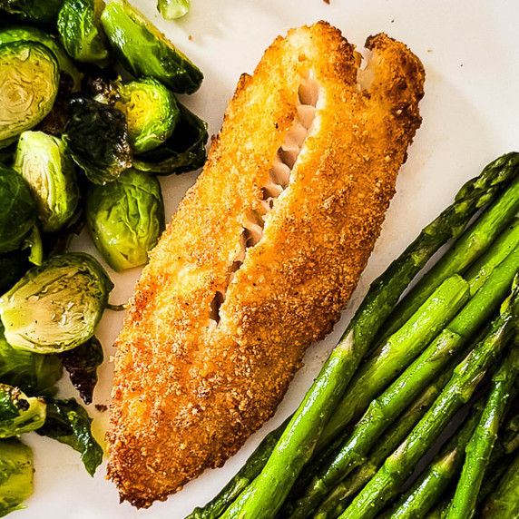 Two crispy tilapia fillets on a dinner plate, ready to serve.