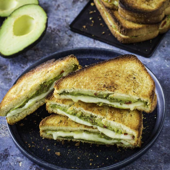 Side shot of multiple triangle halves of avocado grilled cheese on a black plate with more on a blac