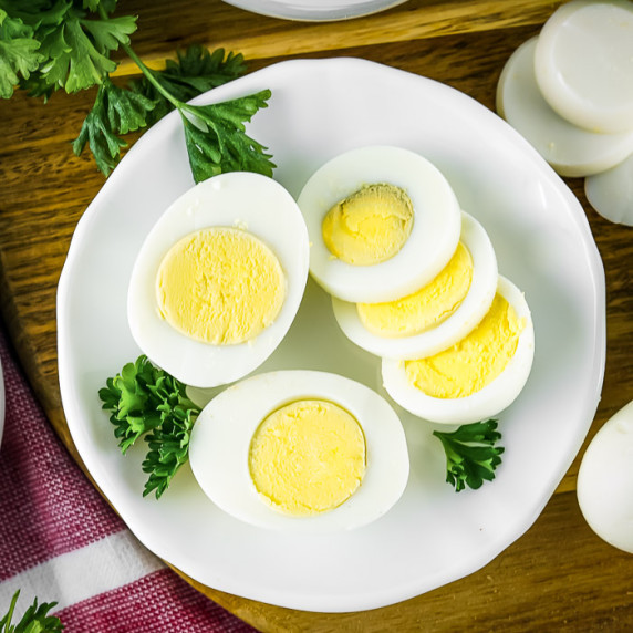 Overhead shot of a few sliced boiled eggs garnished with herbs on a white plate on a wooden surface.